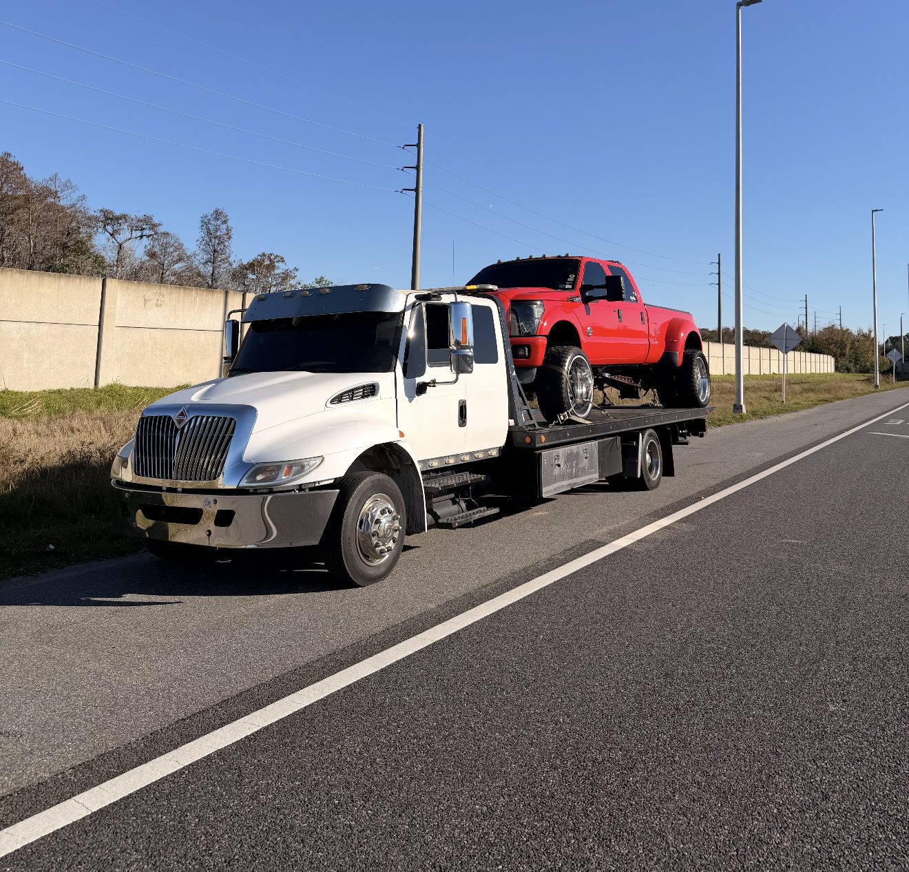A pickup truck secured on a flatbed tow truck under a bright blue sky